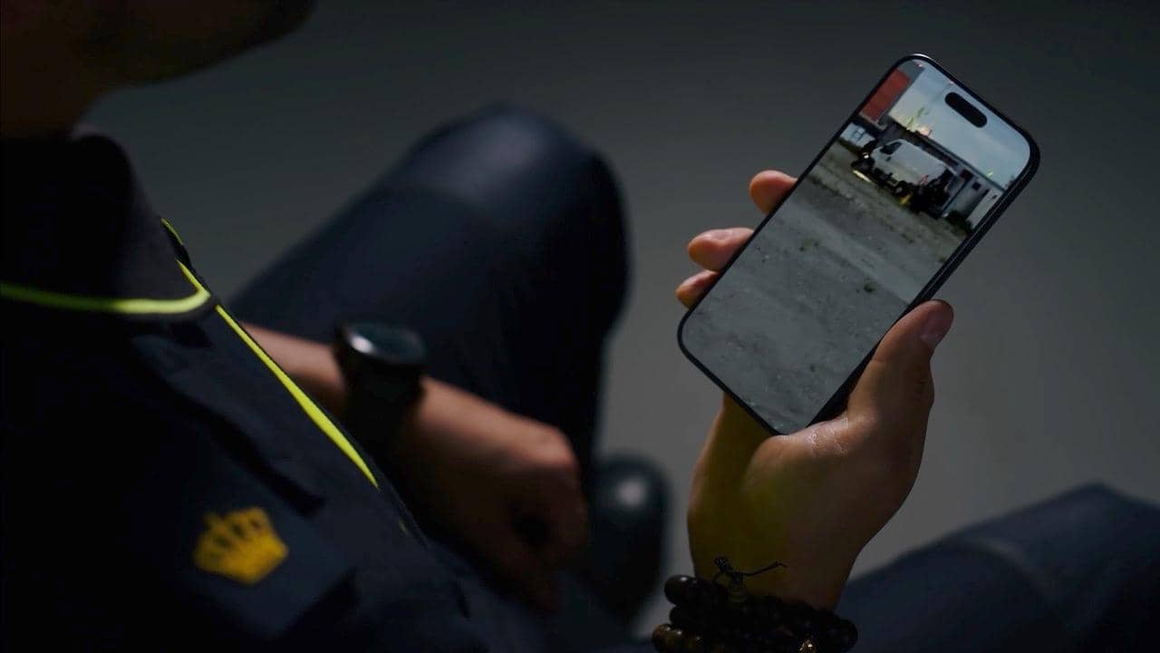 Agent houdt een telefoon in de hand met daarop het beeld van een wit busje.