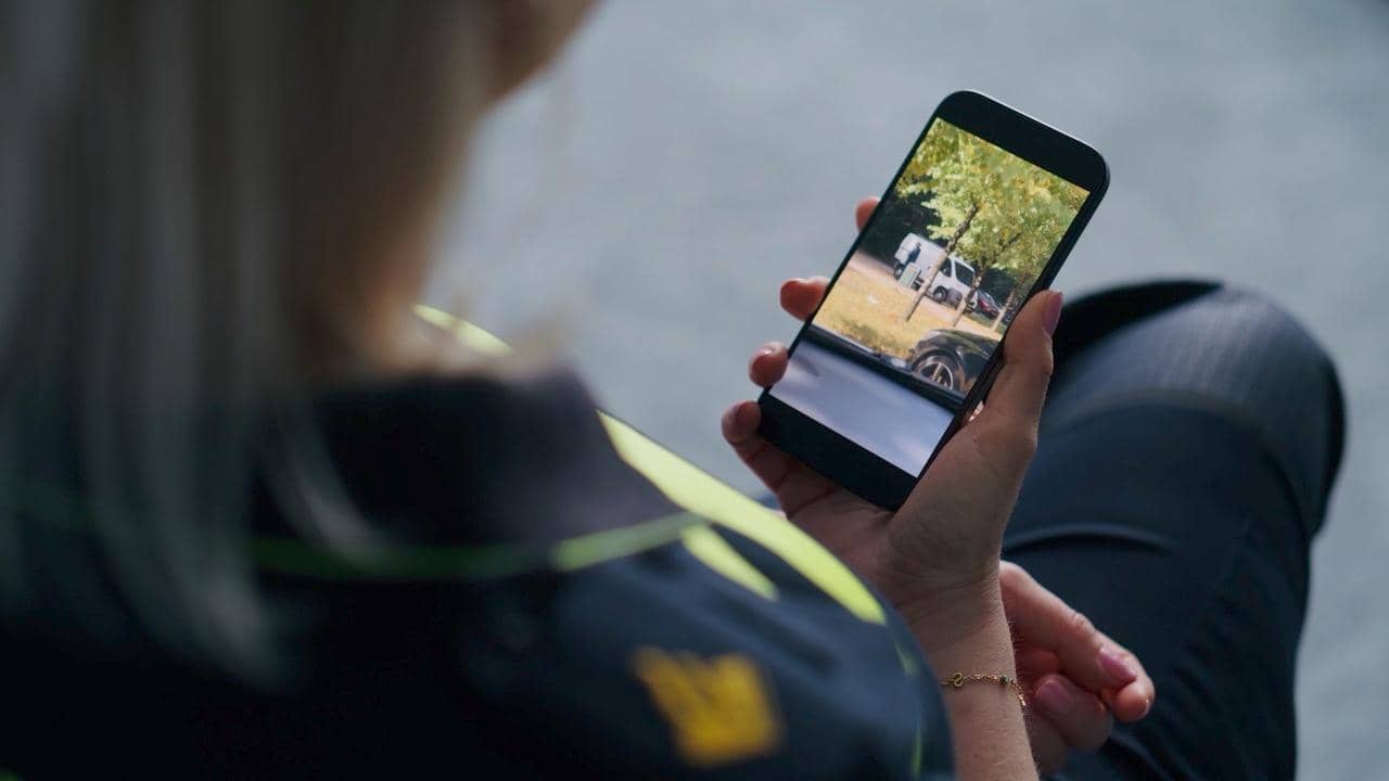 Politieagent houdt een mobiel scherm vast met een verdacht wit busje in beeld.